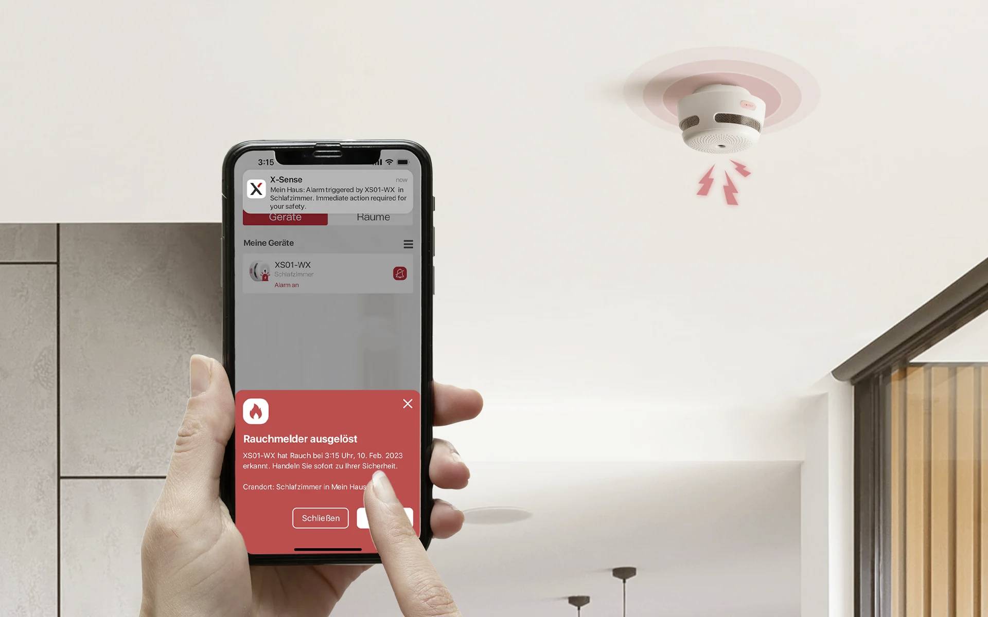 Una persona tiene uno smartphone che mostra un allarme del rilevatore di fumo. Sul soffitto è visibile un rilevatore di fumo attivato.