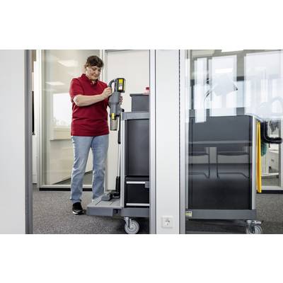 Una persona con una maglietta rossa utilizza un carrello delle pulizie all'interno di un ufficio con pareti di vetro, impugnando un accessorio dell'aspirapolvere, concentrandosi sul mantenimento della pulizia.