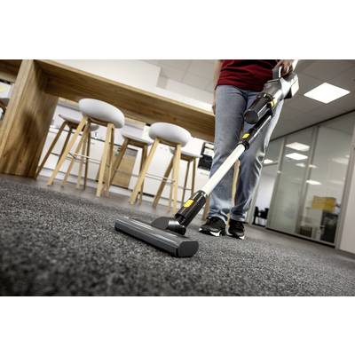 Una persona che aspira un pavimento tappezzato in uno spazio ufficio moderno, con sgabelli e un tavolo di legno sullo sfondo.