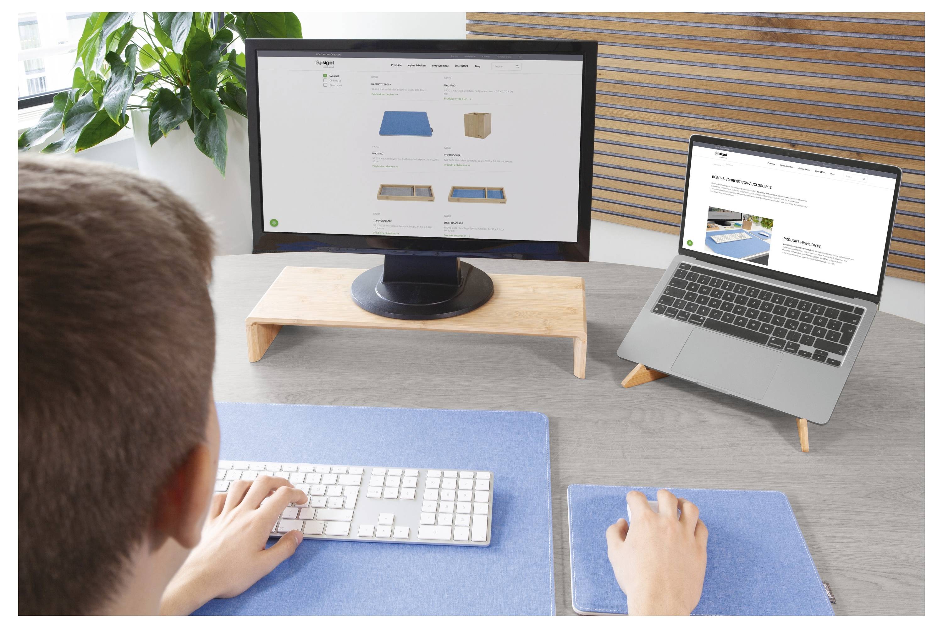 Configurazione desktop con monitor e laptop che visualizzano un sito web di arredamento, mentre una persona utilizza tastiera e mouse su una scrivania.