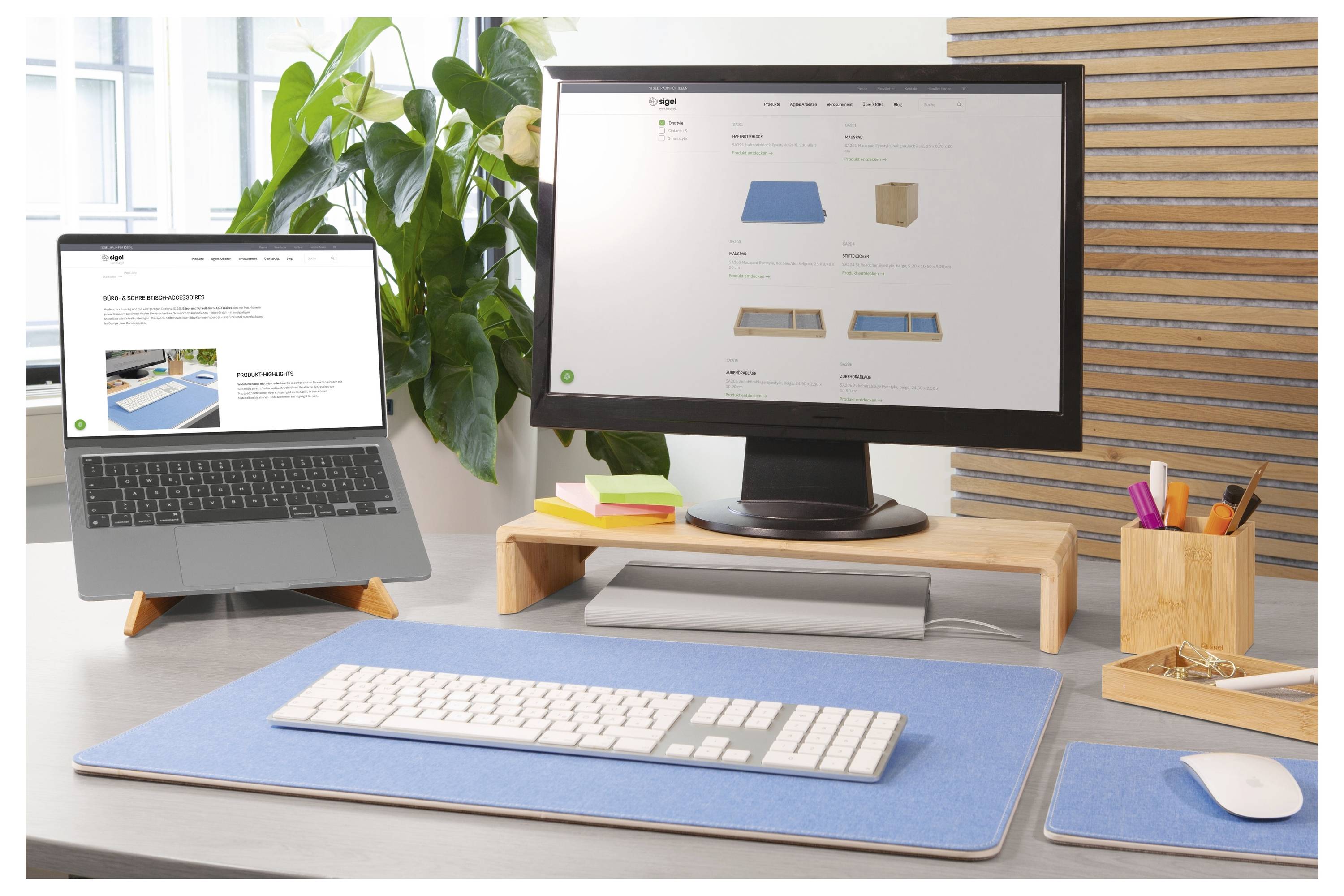 Scrivania moderna per ufficio domestico con un laptop e un monitor che visualizzano un sito web, più tastiera, mouse, piante e accessori da scrivania su uno spazio di lavoro ordinato.