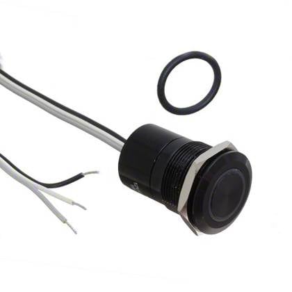 Un pulsante interruttore nero a forma di anello con fili collegati, utilizzato per dispositivi elettronici. Un anello O-ring è posizionato accanto ad esso, probabilmente per la tenuta ermetica.