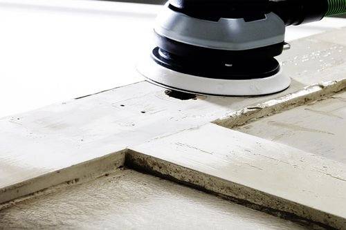 Un'immagine ravvicinata di un utensile per levigare che sta lisciando una superficie in legno bianco, rimuovendo strati di vecchia vernice per un progetto di rifinitura.