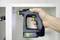 Una persona usa un trapano senza fili per avvitare una vite in un mobile bianco. Il trapano è nero con dettagli verdi e riporta la scritta 'FESTOOL 12V'.