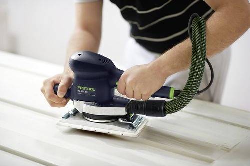 Una persona che utilizza una levigatrice elettrica per levigare una superficie in legno, impugnando saldamente lo strumento con entrambe le mani in un ambiente di lavoro.