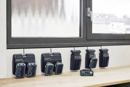 Più caricabatterie e batterie sono allineati su una scrivania di legno sotto una finestra, con alcuni montati al muro per la ricarica.
