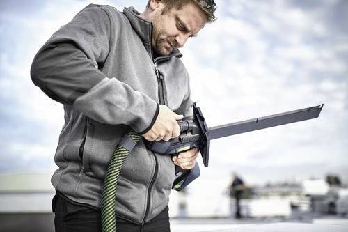 Una persona usa una sega all'aperto, concentrata intensamente, indossando una giacca grigia. Il cielo è nuvoloso, suggerendo una giornata frizzante.