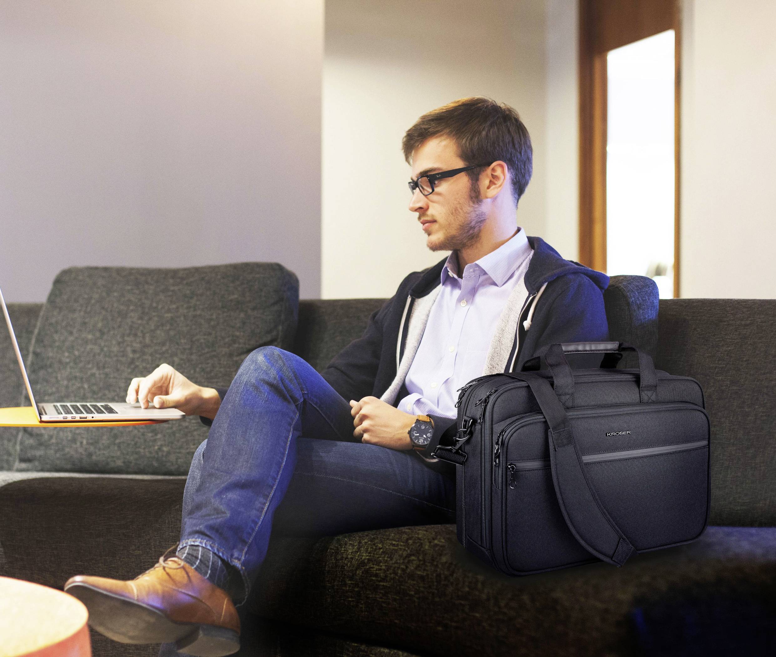 Uomo seduto su un divano che utilizza un laptop con una borsa per laptop nera accanto a sé.