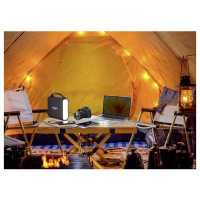 All'interno di una tenda illuminata, un tavolo contiene un portatile, una fotocamera, un power bank e un tablet. Le lanterne forniscono una luce calda, creando un'accogliente configurazione da campeggio.