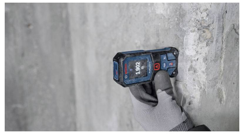 Una persona che indossa un guanto utilizza un misuratore di distanza digitale contro un muro di cemento. Il dispositivo mostra '1.902'.