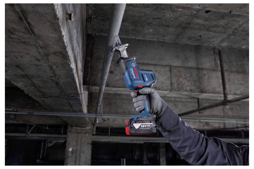 Una persona che utilizza una sega elettrica cordless blu e rossa per tagliare un tubo metallico su un soffitto in un contesto industriale.