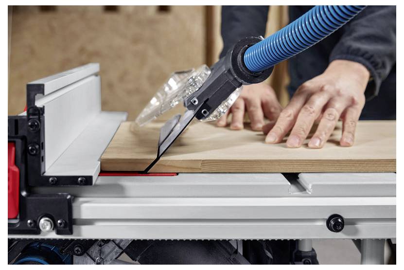 Una persona sta utilizzando una sega circolare da banco per tagliare una tavola di legno, con le mani che guidano la tavola lungo la linea di taglio. Sono visibili le caratteristiche di sicurezza.