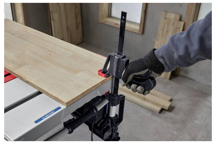 Una persona che indossa guanti utilizza una pinza per fissare un'asse di legno su un banco da lavoro in un ambiente di officina.