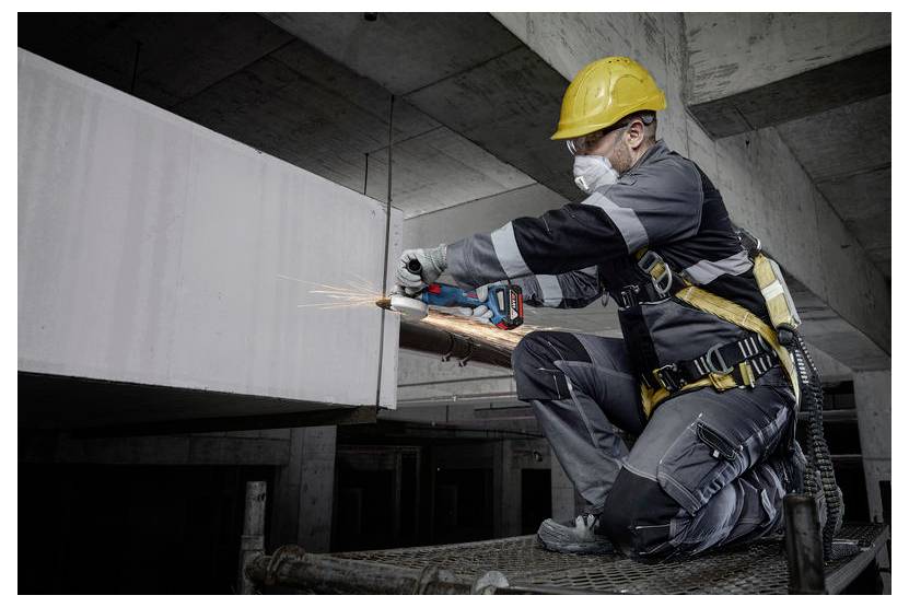 Lavoratore con dispositivi di protezione personale e casco che utilizza un utensile elettrico portatile per tagliare il metallo, con scintille che volano, in un ambiente industriale.