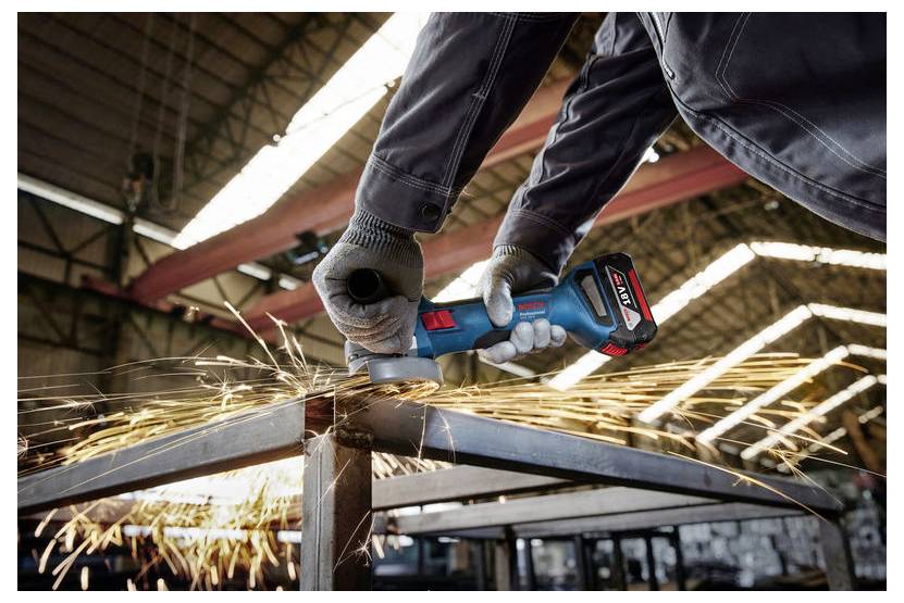 Una persona lavora un metallo con un utensile elettrico, facendo schizzare scintille. Indossa guanti protettivi all'interno di un laboratorio industriale.