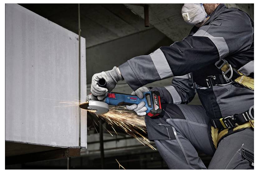 Un lavoratore edile con indumenti di sicurezza utilizza un utensile elettrico per tagliare il metallo, producendo scintille. Il lavoratore è concentrato e indossa dispositivi di protezione individuale.