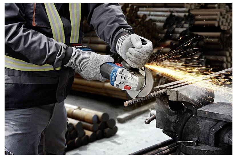 Una persona che indossa dispositivi di protezione utilizza un smerigliatrice angolare per tagliare barre metalliche, con scintille che volano in un ambiente di officina industriale.