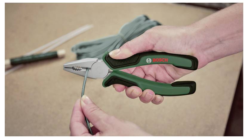 Una persona usa pinze a becco sottile Bosch per tagliare un filo verde. Un fascio di fili e una penna sono visibili sullo sfondo di un tavolo.
