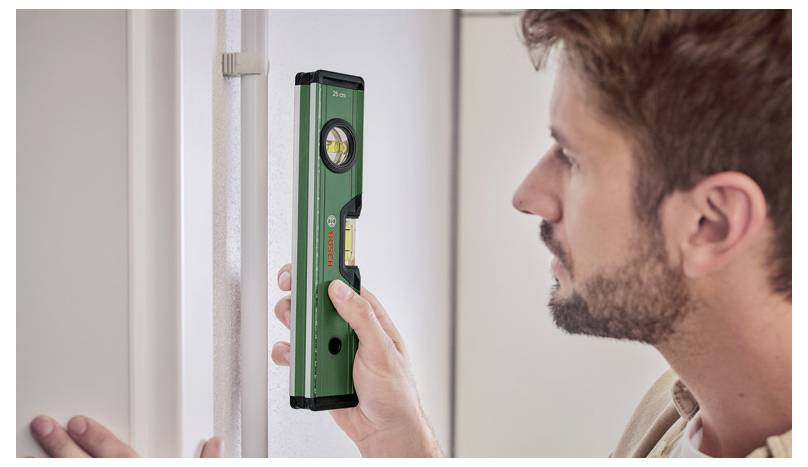 Una persona utilizza un livello a bolla verde contro un muro per garantire l'allineamento. Concentrarsi sulla bolla orizzontale dello strumento, che indica l'equilibrio.