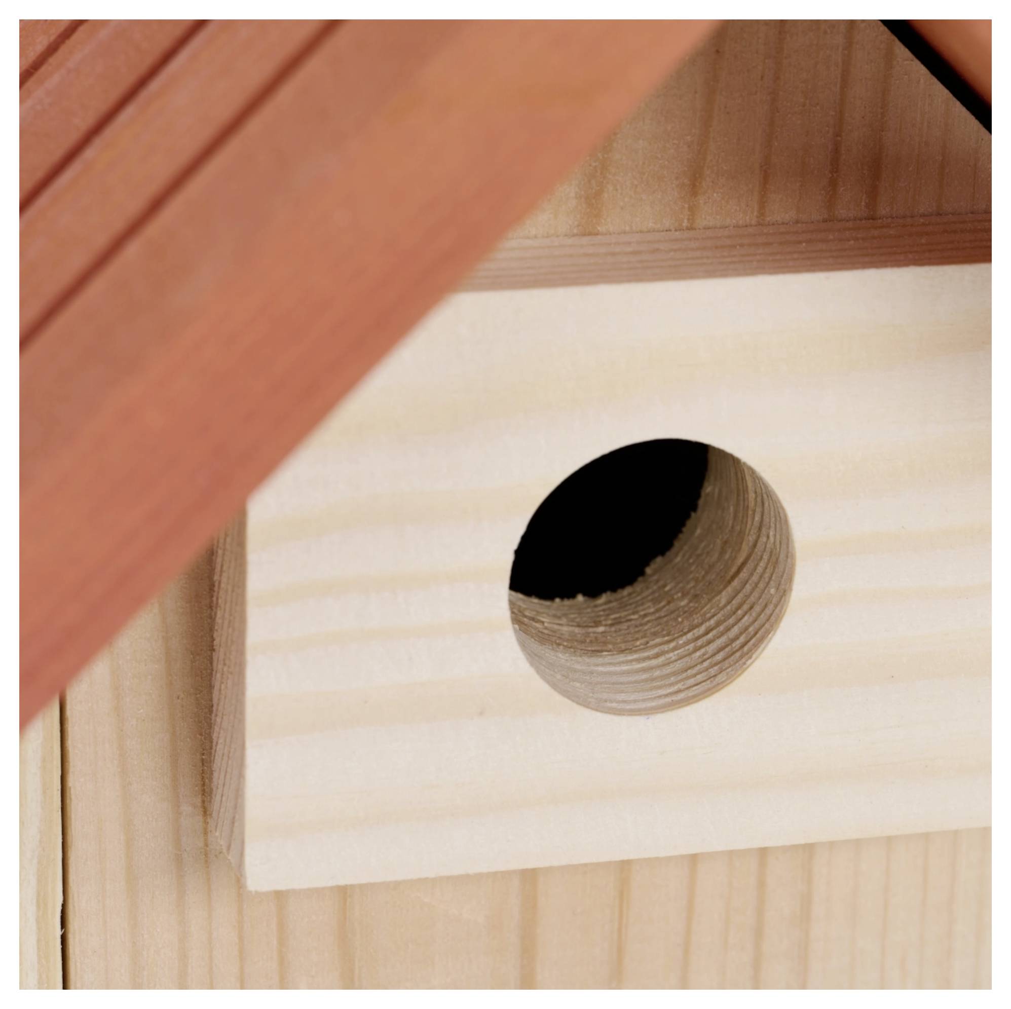 Una casetta per uccelli in legno con un ingresso circolare è attaccata a una struttura in legno con un tetto inclinato sopra di essa.