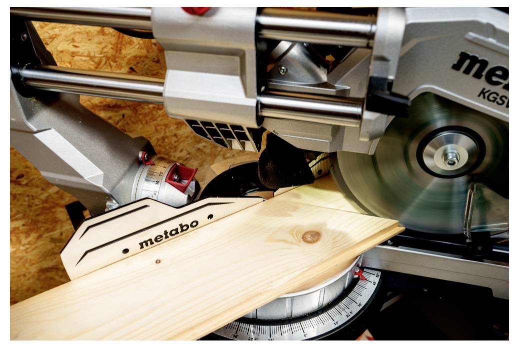 Sega da taglio 'Metabo' che taglia una tavola di legno ad angolo. Vista ravvicinata, che evidenzia il contatto tra lama e legno.