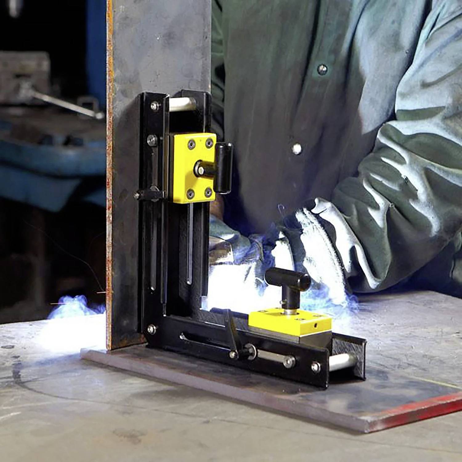 Una persona che indossa una giacca da saldatura sta utilizzando un supporto magnetico per saldatura su un pezzo di metallo in un laboratorio, con scintille visibili durante il processo.