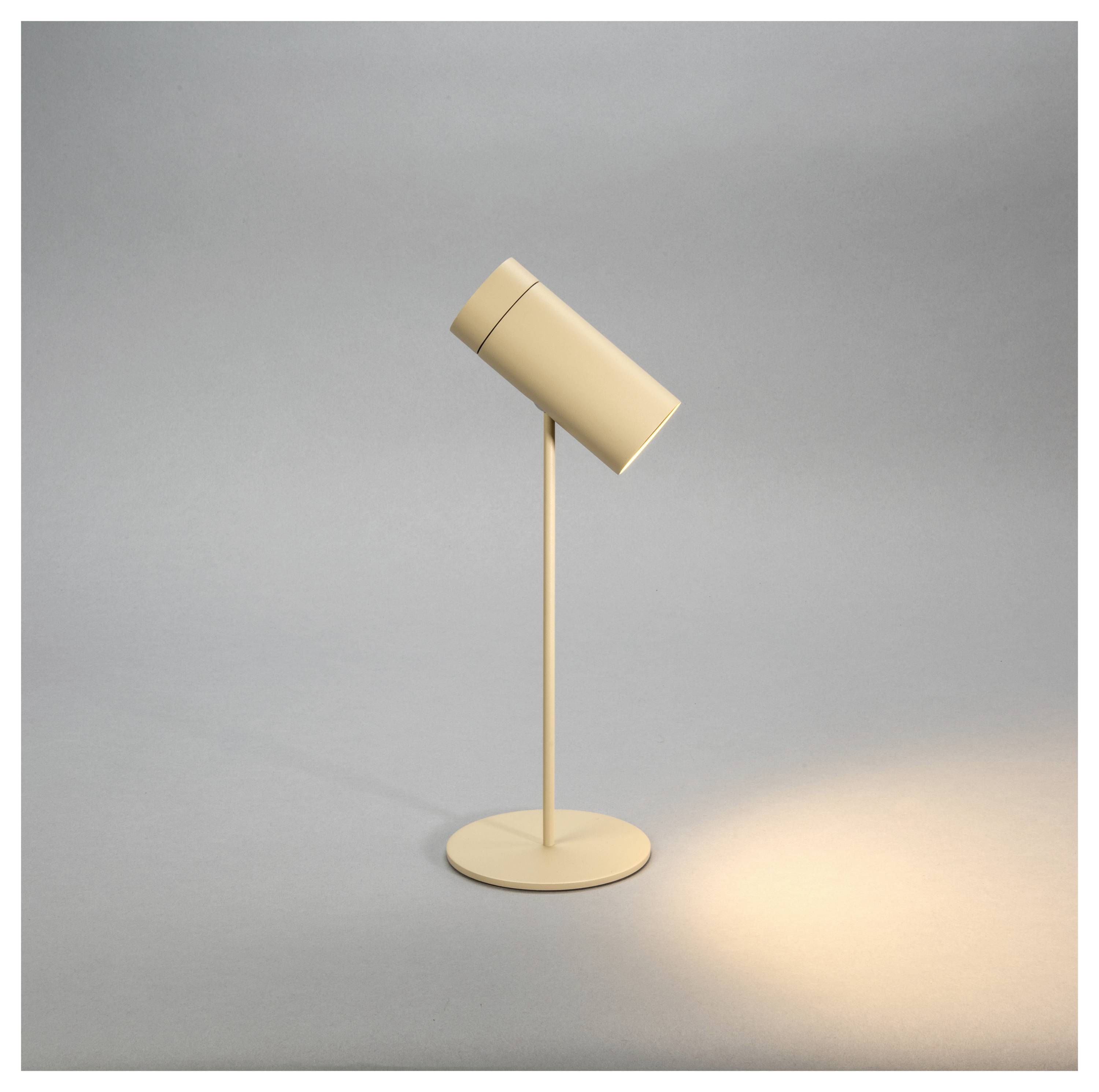 Una lampada da tavolo elegante e moderna in beige, con un paralume cilindrico, proietta la luce su una superficie grigia, creando un bagliore morbido e concentrato.