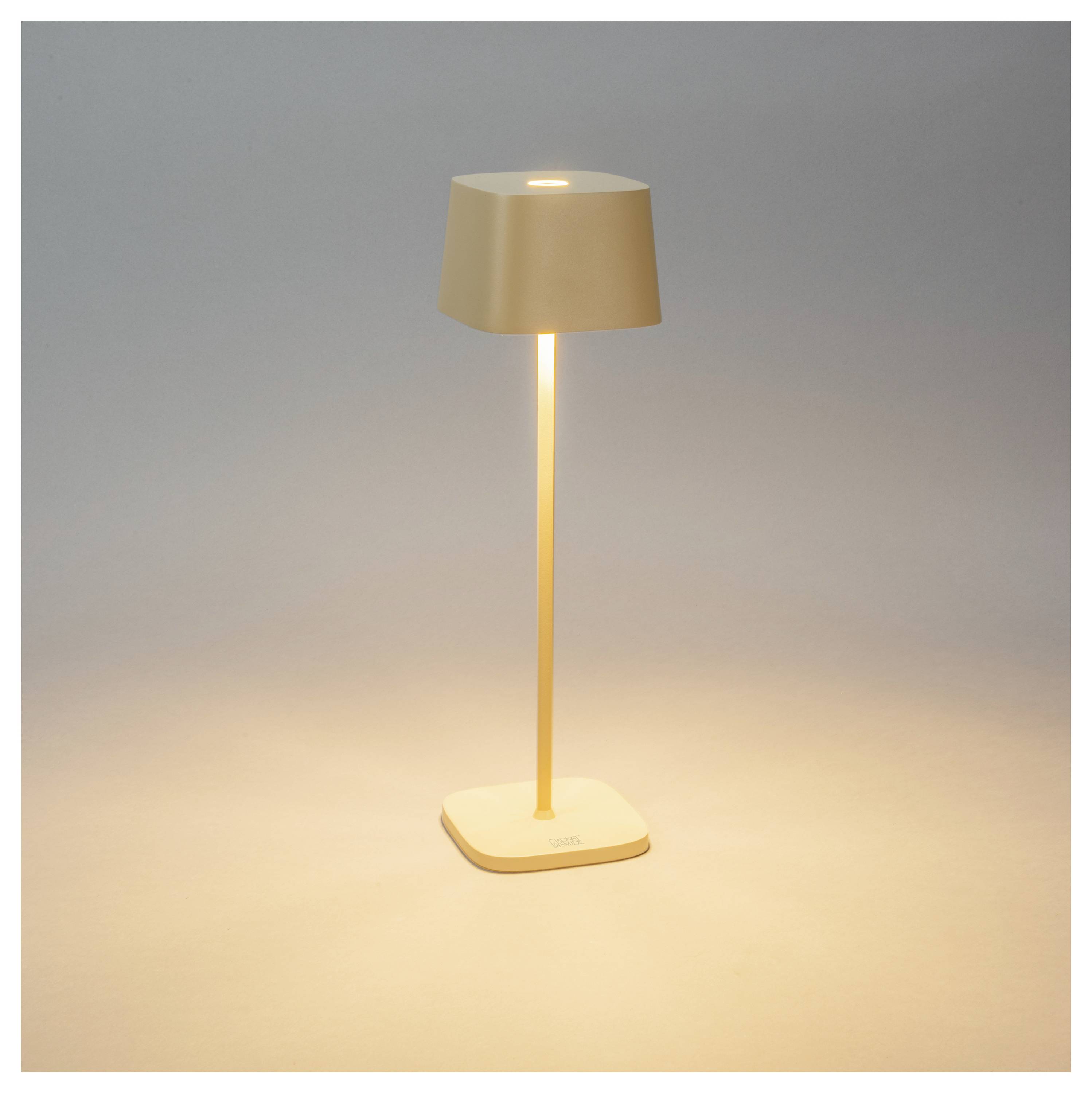 Una lampada da tavolo moderna e minimalista con uno stelo sottile e un paralume rettangolare, che proietta un bagliore caldo sulla sua base quadrata e sull'area circostante.