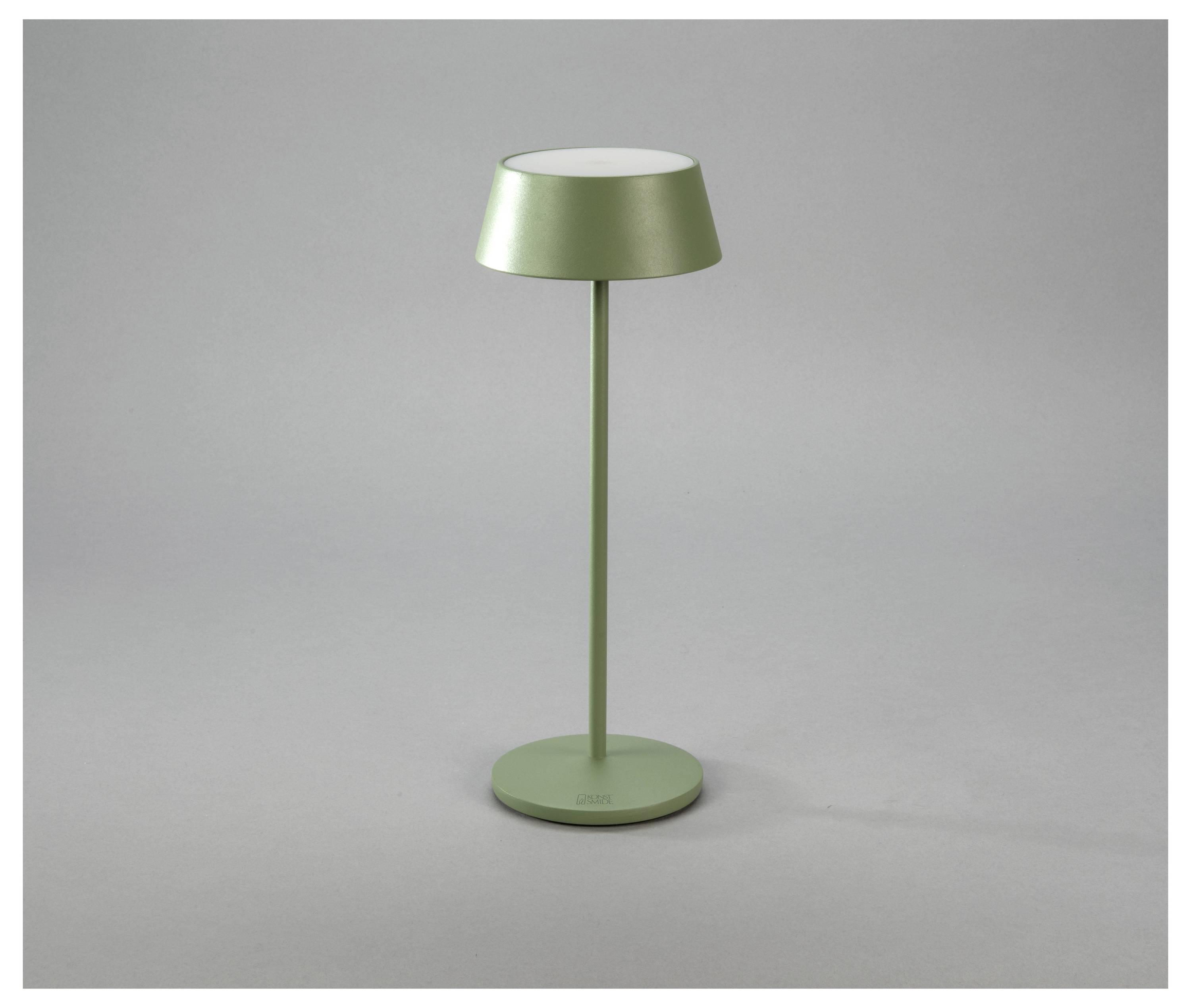 Una lampada da tavolo moderna e verde con base cilindrica e paralume ampio e piatto, poggia su uno sfondo grigio neutro.