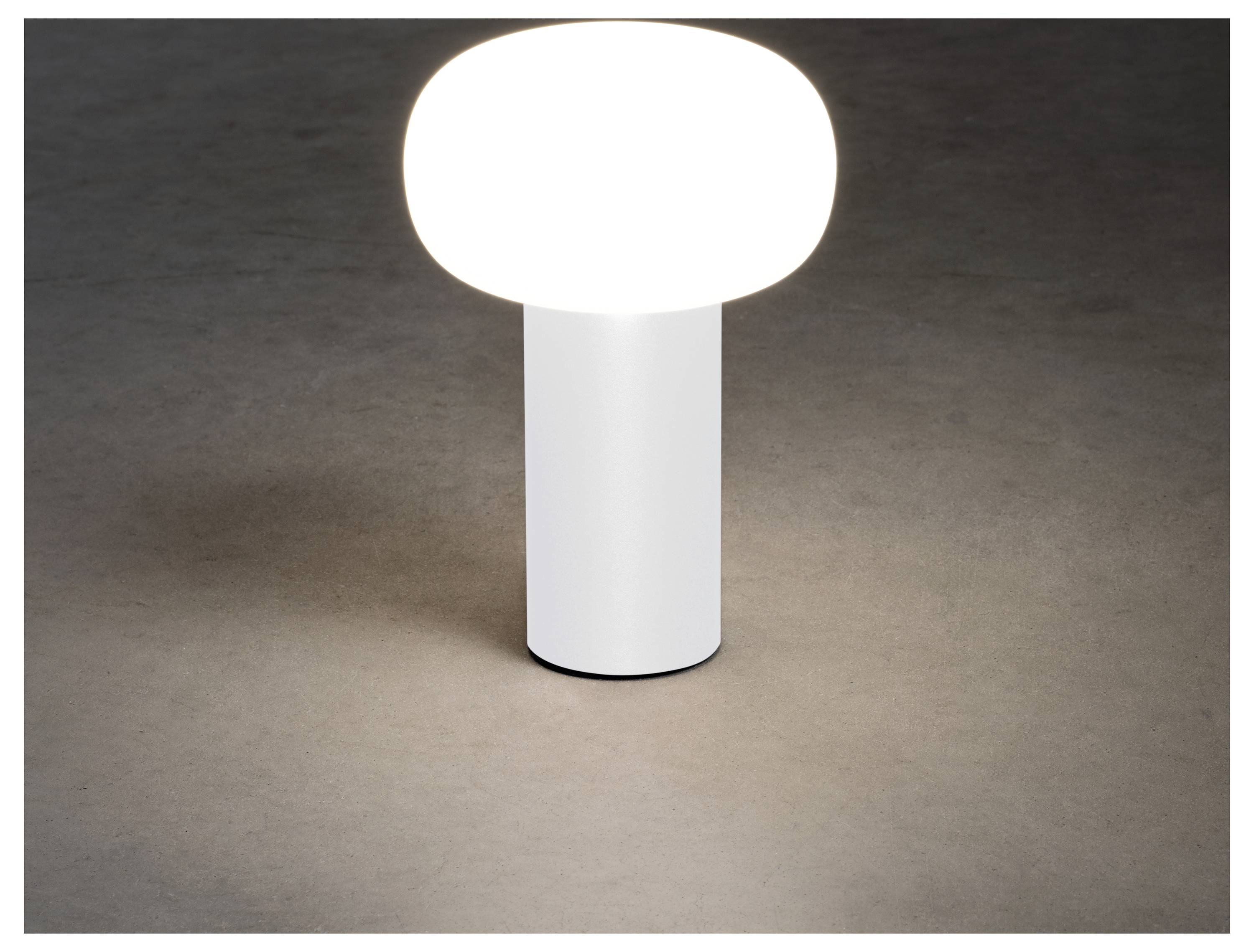 Una lampada da tavolo moderna con base cilindrica e parte superiore ovale che emette una luce bianca soffusa su una superficie scura.