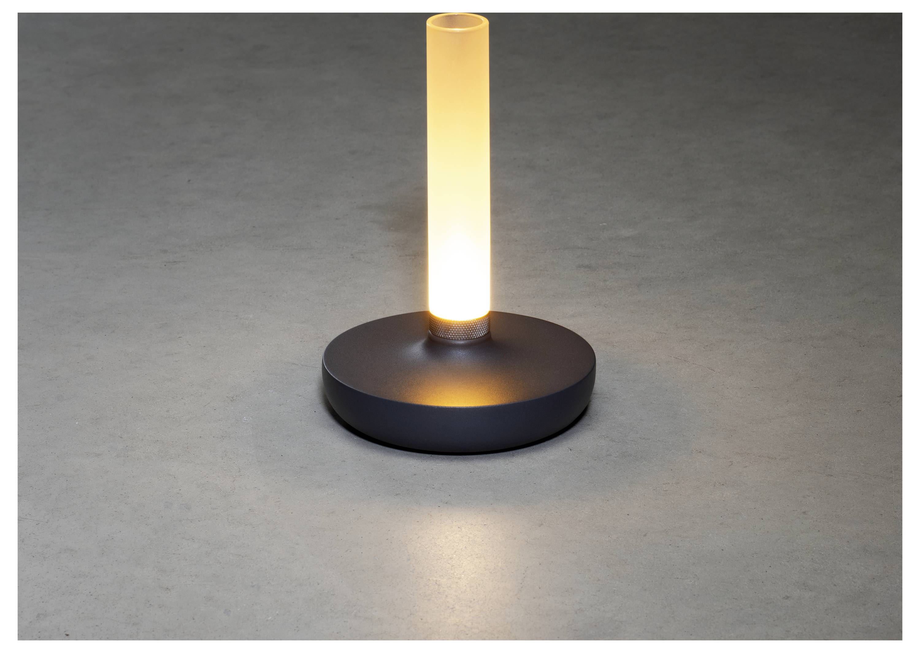 Una lampada cilindrica moderna emette una luce soffice e calda, posizionata su una superficie liscia e grigia.