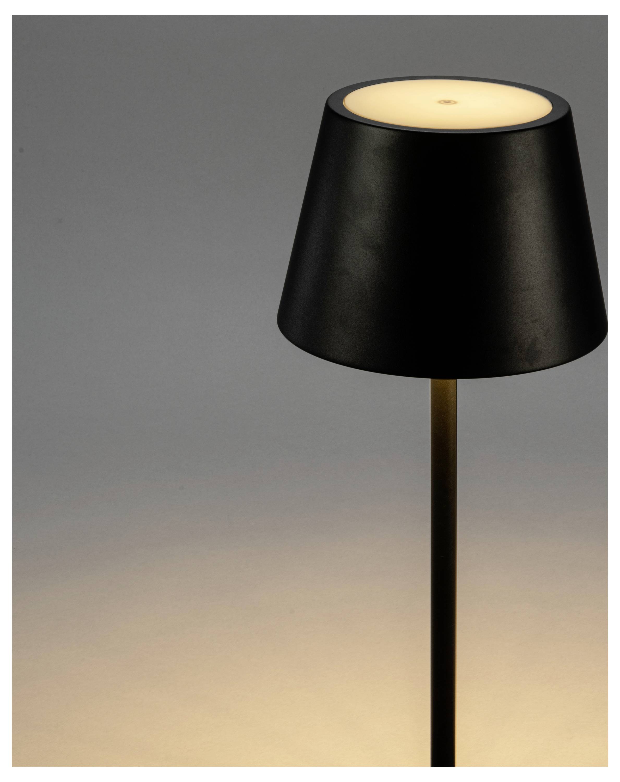 Una moderna lampada da terra nera dal design minimalista emette una luce calda e soffusa in uno spazio scarsamente illuminato, creando un'atmosfera accogliente.