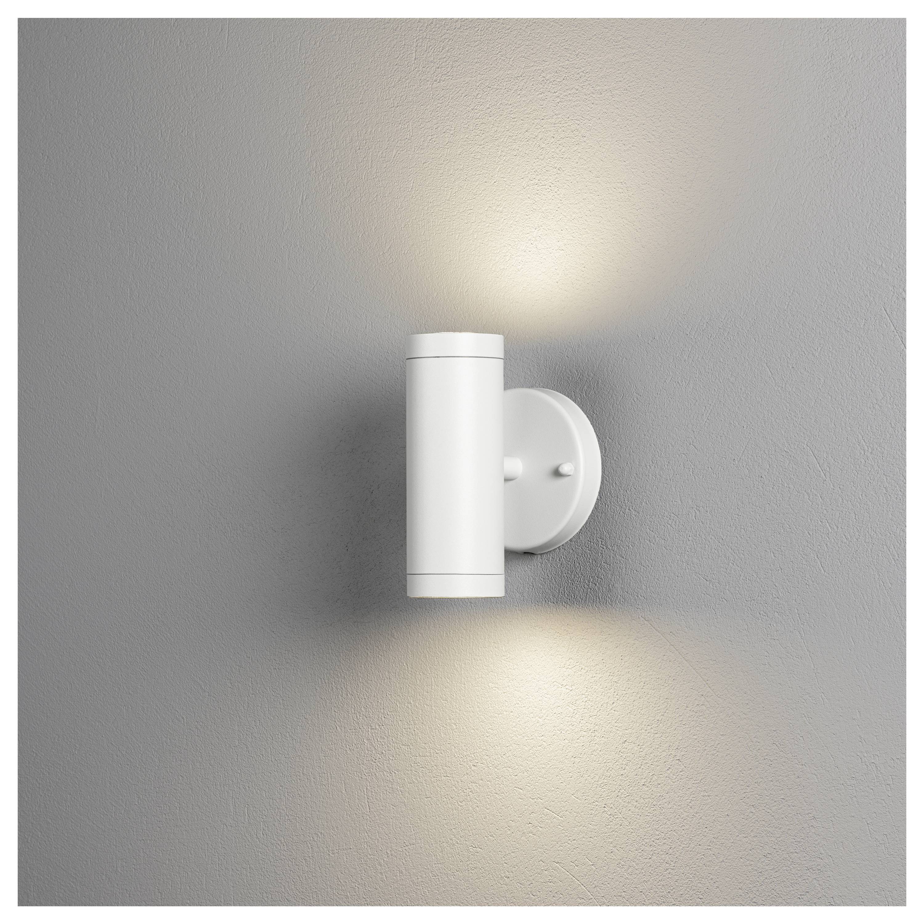 Un applique cilindrico bianco emette luce verso l'alto e verso il basso, montato su una parete grigia, creando un bagliore soft per un'illuminazione ambientale.