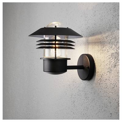 Un applique moderno nero con barre metalliche orizzontali che circondano una lampadina di vetro trasparente, che emette una luce calda su una parete grigia testturata.