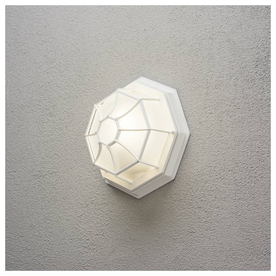 Un apparecchio di illuminazione da parete geometrico, ottagonale, emette un bagliore soffice contro una parete grigia testurizzata. Il design ricorda un motivo a ragnatela.