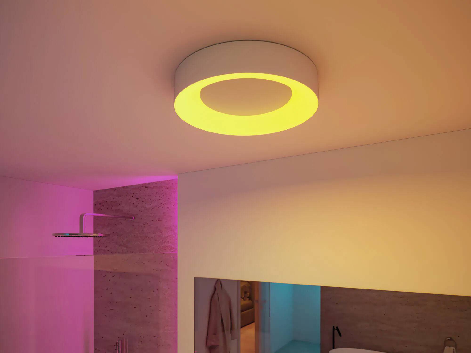 Un bagno moderno presenta un lampadario circolare sul soffitto che emana un bagliore caldo. La stanza è delicatamente illuminata con tonalità rosa e gialle.