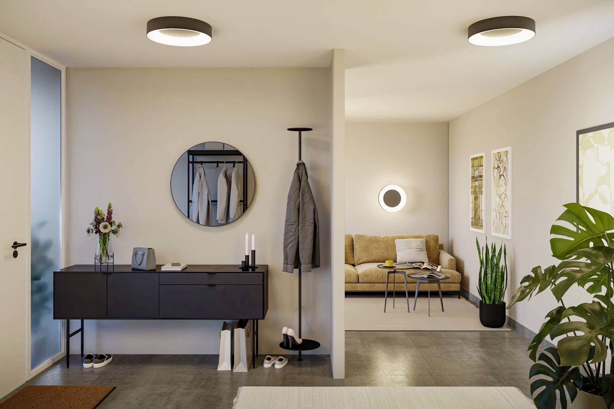 Un ingresso di un appartamento moderno e minimalista con uno specchio rotondo, un appendiabiti, e una vista sul soggiorno con un divano e delle piante.