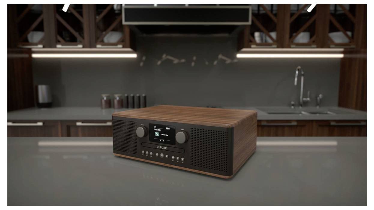 Una radio digitale in legno con display e manopole di controllo è posizionata su un piano di lavoro moderno in cucina, sullo sfondo si vedono eleganti armadietti e un lavandino.