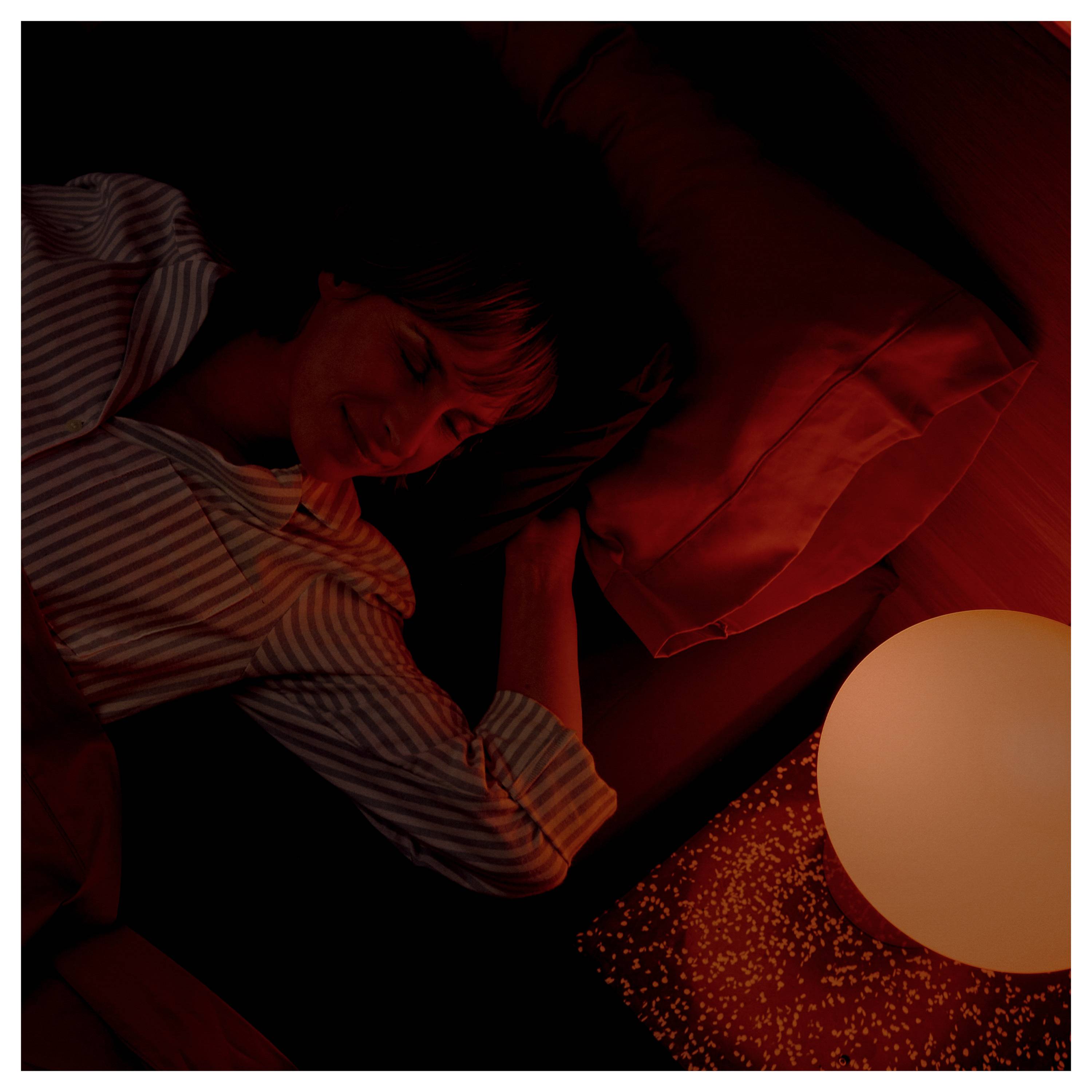 Una persona dorme pacificamente in una stanza semibuia con una lampada sferica luminosa nelle vicinanze, che proietta una luce calda e arancione sul letto e sul cuscino.