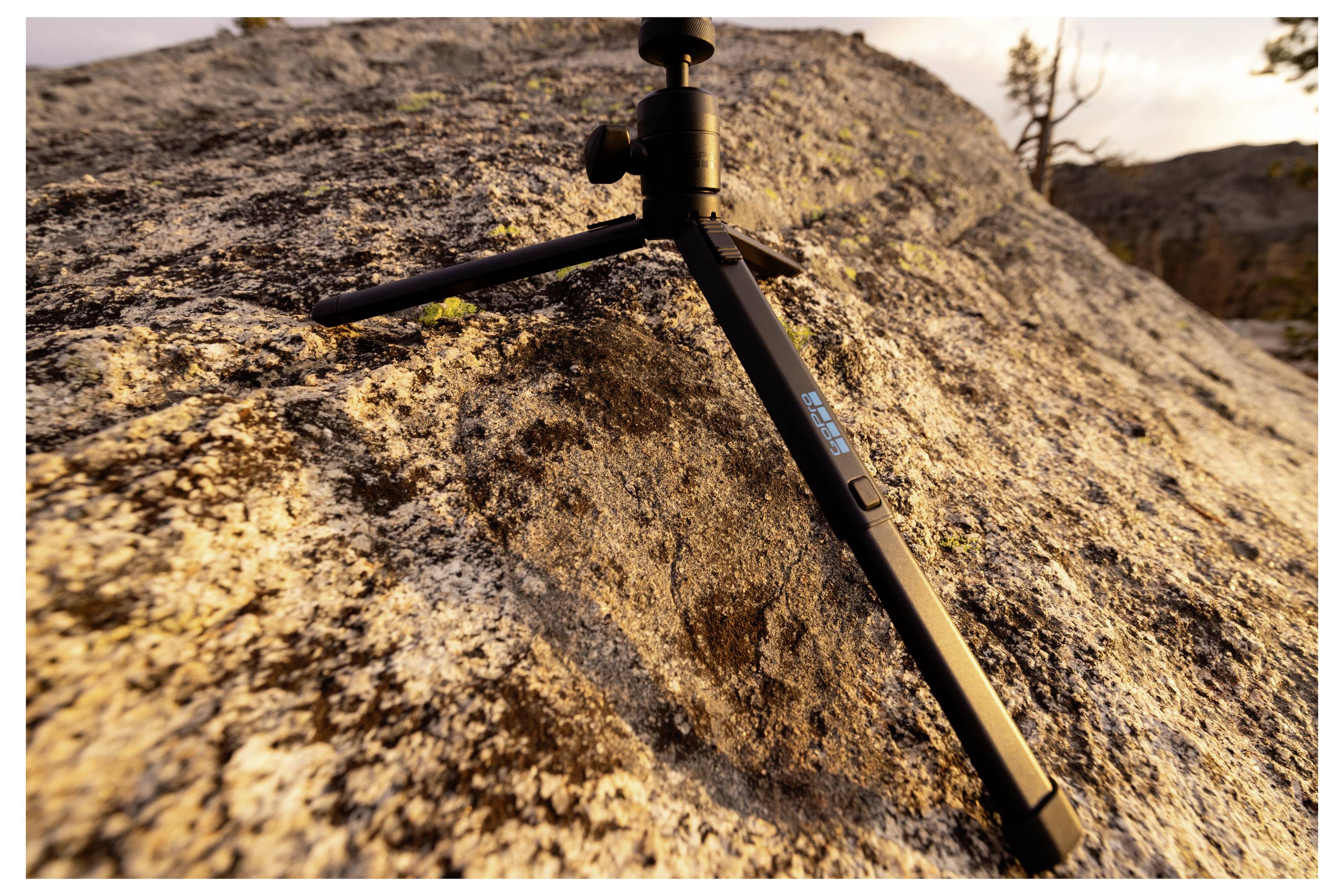 Un treppiede nero è posizionato su una grande roccia in un ambiente esterno, suggerendo il suo utilizzo per stabilizzare una fotocamera in un terreno accidentato.