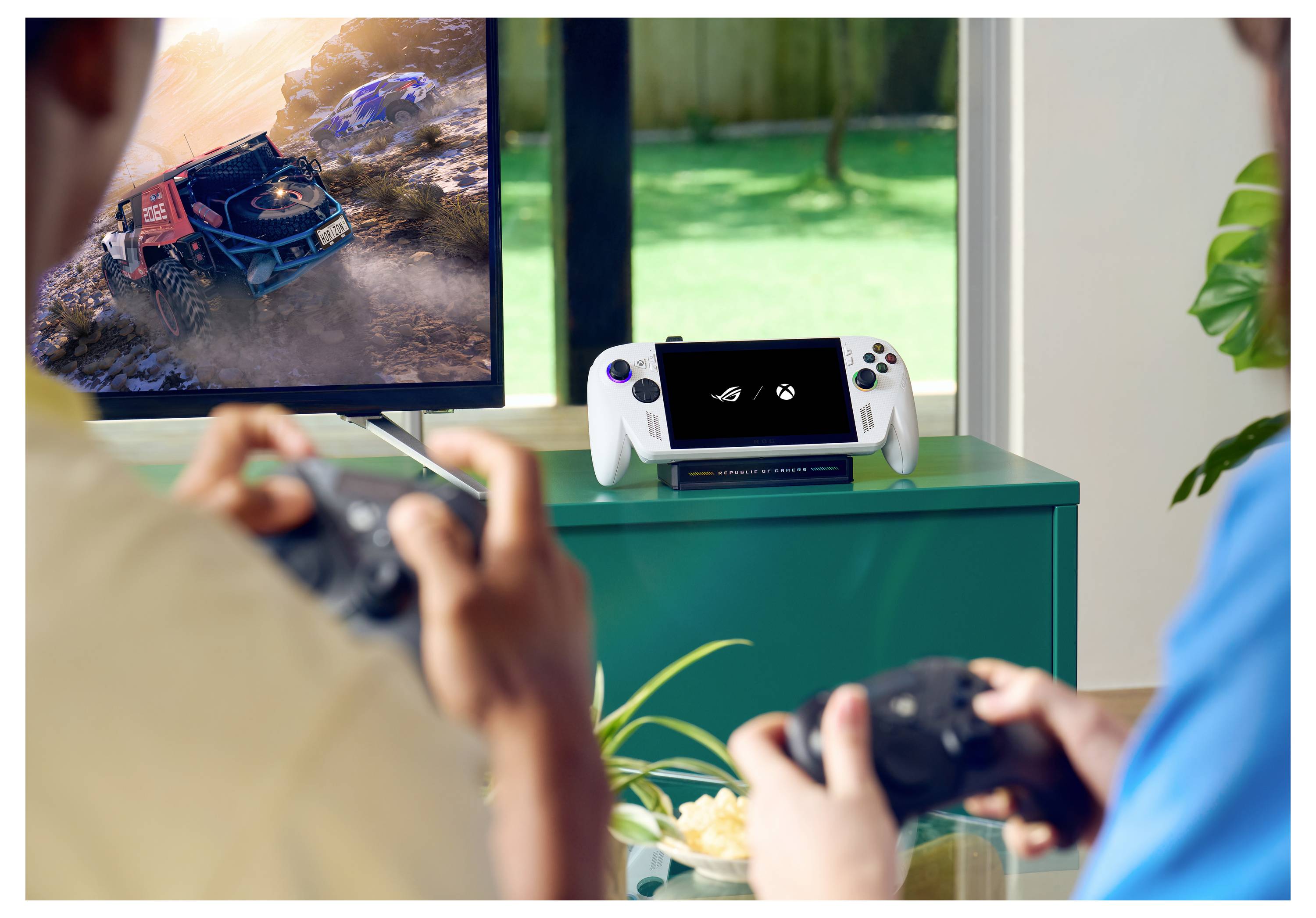 Due persone che giocano a videogiochi su una console con i controller; una TV mostra un gioco di corse, e un dispositivo portatile è posizionato nelle vicinanze.
