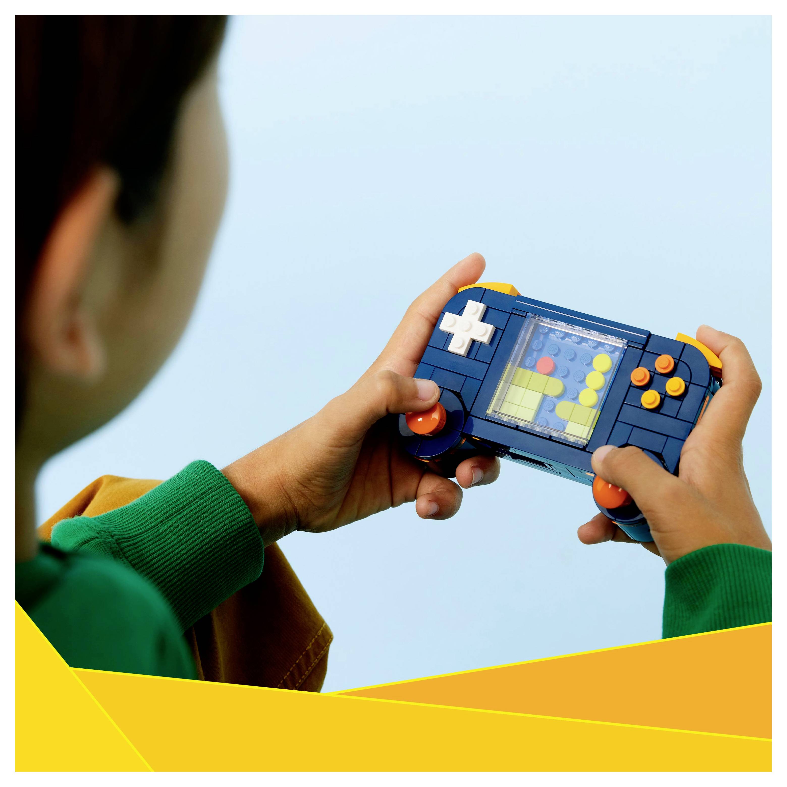 Una persona sta tenendo in mano un dispositivo portatile da gioco colorato e simile a un giocattolo, con bottoni visibilmente rossi, bianchi e gialli, in una stanza illuminata.