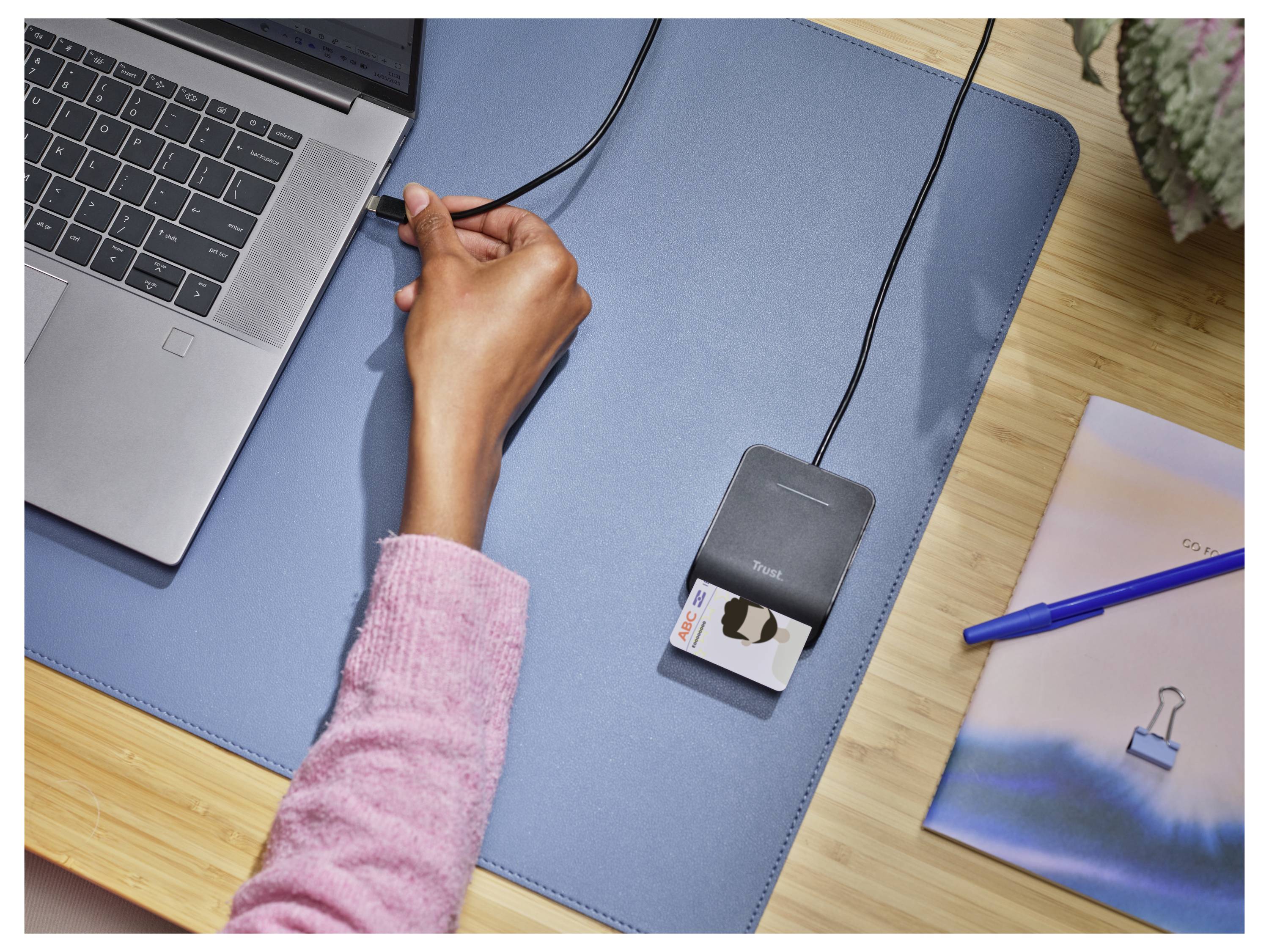 Una persona collega un cavo USB a un laptop accanto a un lettore di carte d'identità su una scrivania, evidenziando l'azione di configurazione o utilizzo del lettore di carte.