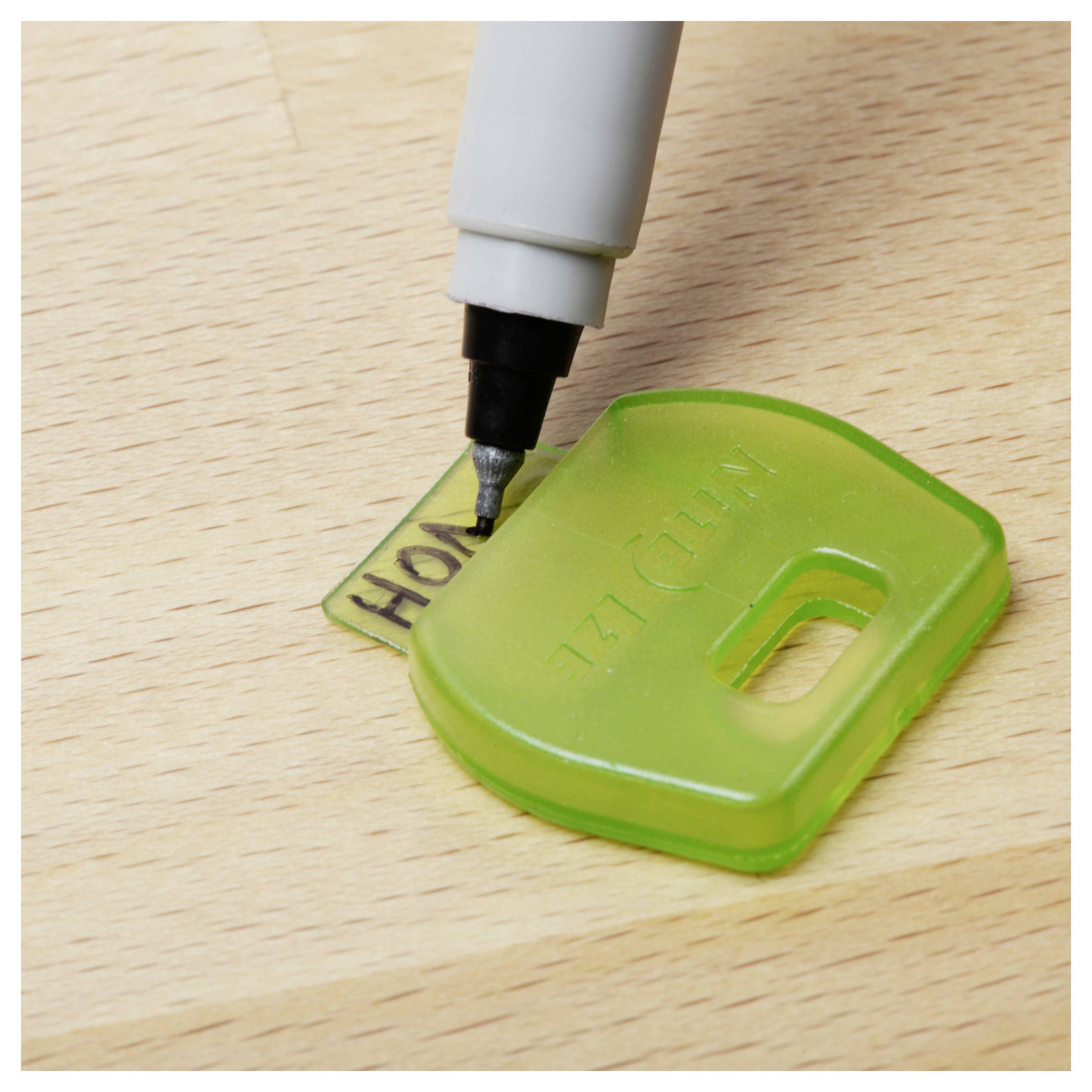 Un pennarello nero che etichetta un portachiavi verde con la parola 'HOME' su una superficie di legno.