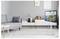 Un soggiorno moderno con un divano grigio, un tavolino da caffè bianco, una TV montata a parete che mostra un'immagine panoramica di una costa, e un arredamento minimalista.