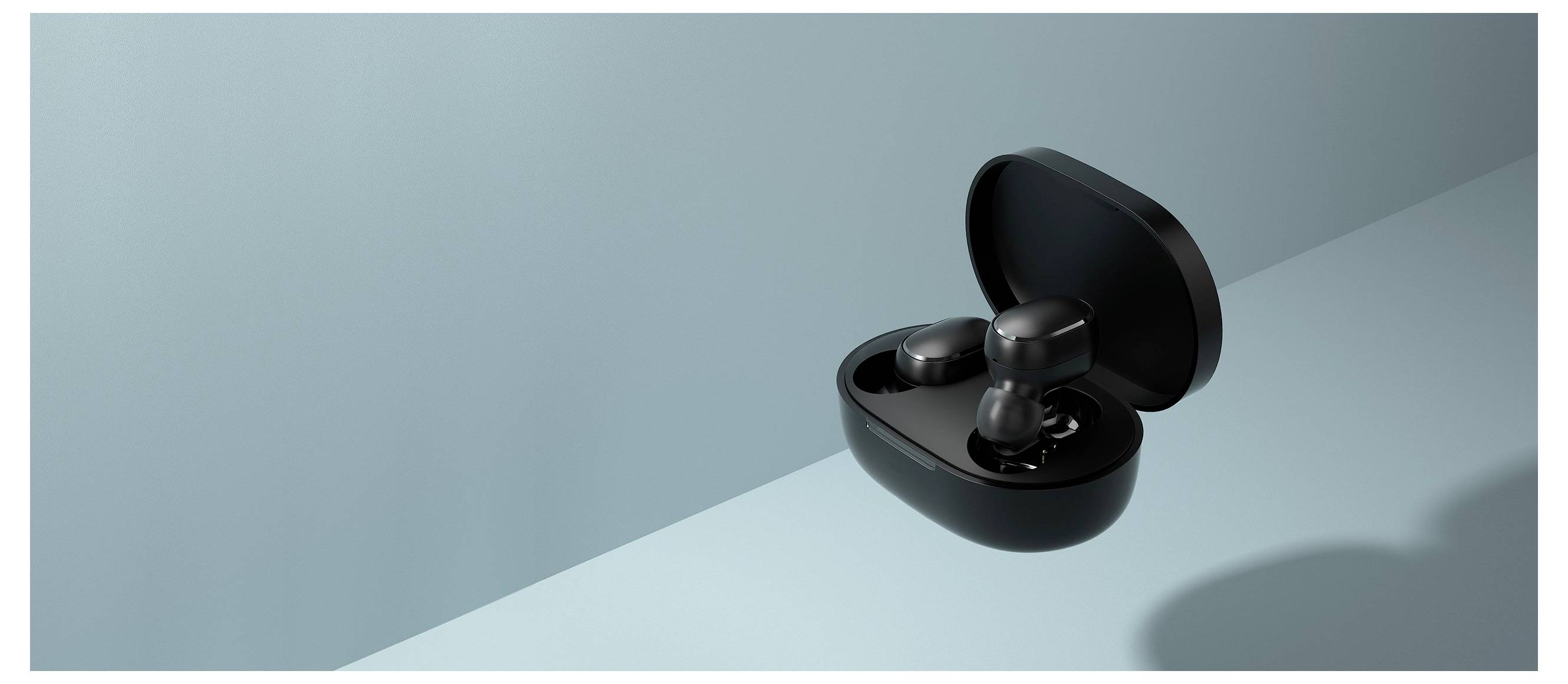 Custodia aperta di auricolari wireless neri con gli auricolari all'interno su una superficie azzurro chiaro. Le ombre proiettate sulla superficie aggiungono profondità.