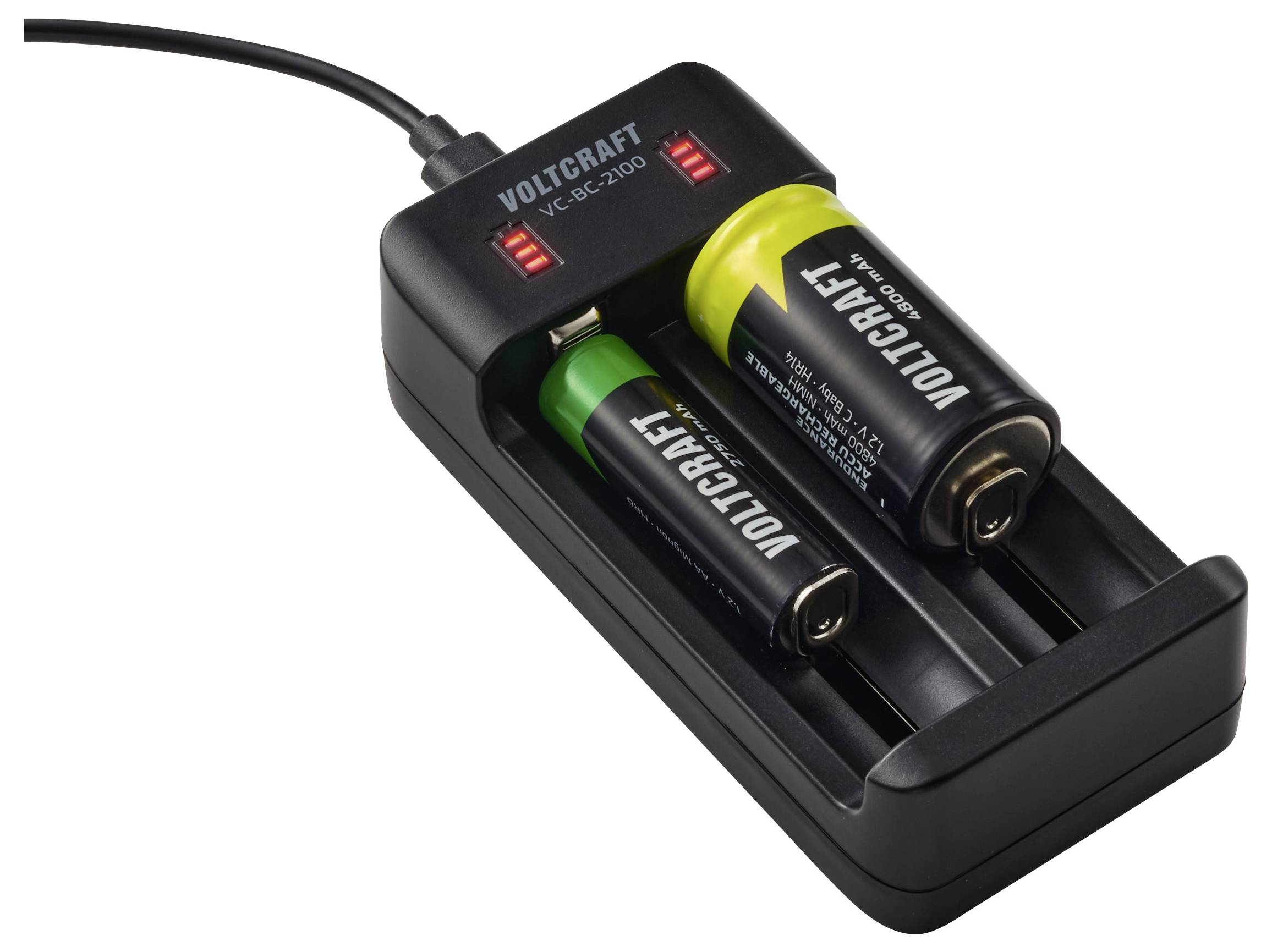 Un caricabatterie etichettato 'Voltcraft' carica due batterie AA, una con un involucro verde e una con un involucro giallo, collegato a una fonte di alimentazione.