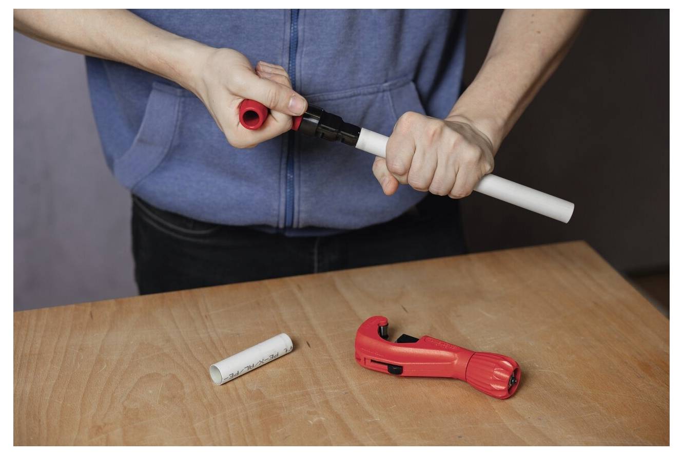 Persona con felpa blu che utilizza un attrezzo per connettere tubi in PVC su un tavolo di legno, con un tagliatubi nelle vicinanze.