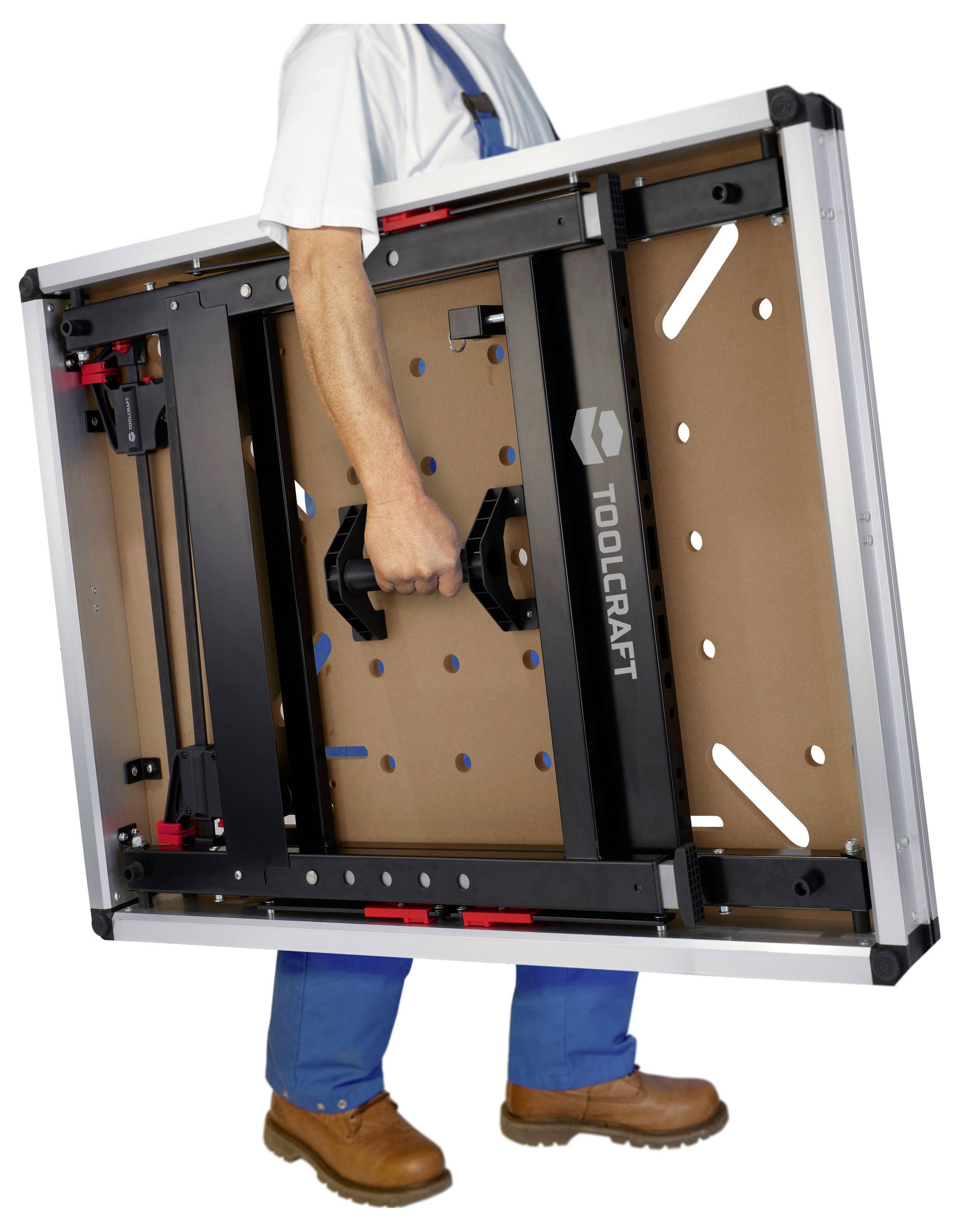 Persona che trasporta un banco da lavoro Toolcraft ripiegato per il suo manico centrale, mostrando il telaio portatile compatto.