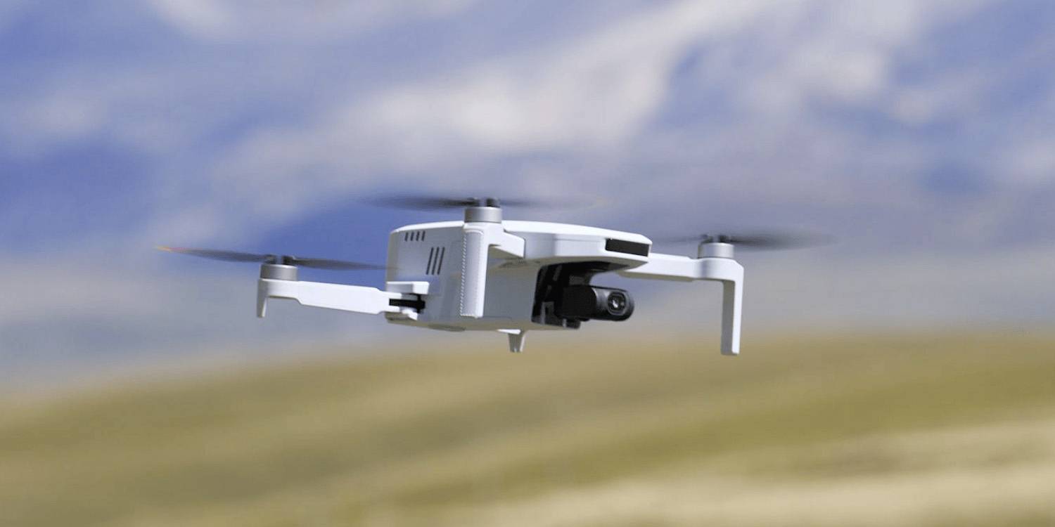 Un drone bianco che vola sopra un paesaggio sfocato, con montagne sullo sfondo, che mette in mostra il suo design e la capacità di fotografia aerea.
